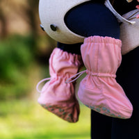 Pink baby shoes with a blurred background of greenery
